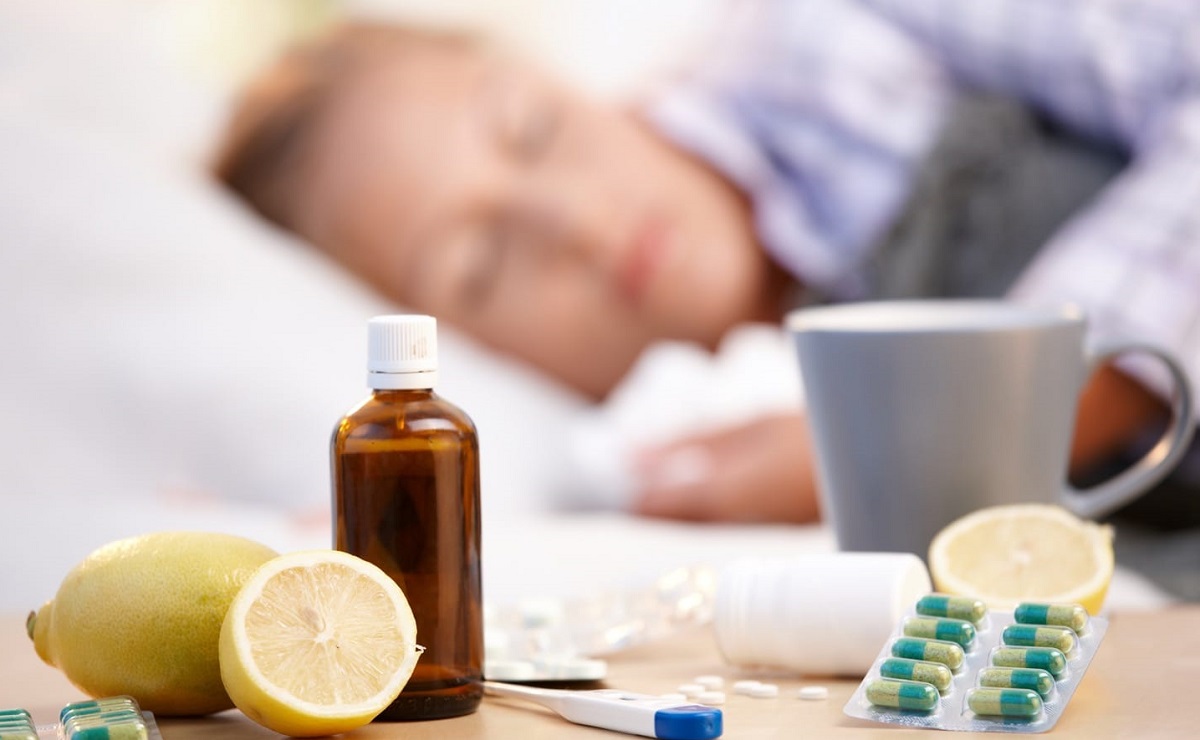 Vitamins-medicines-and-hot-tea-in-front-of-woman-with-a-cold-sleeping-in-background